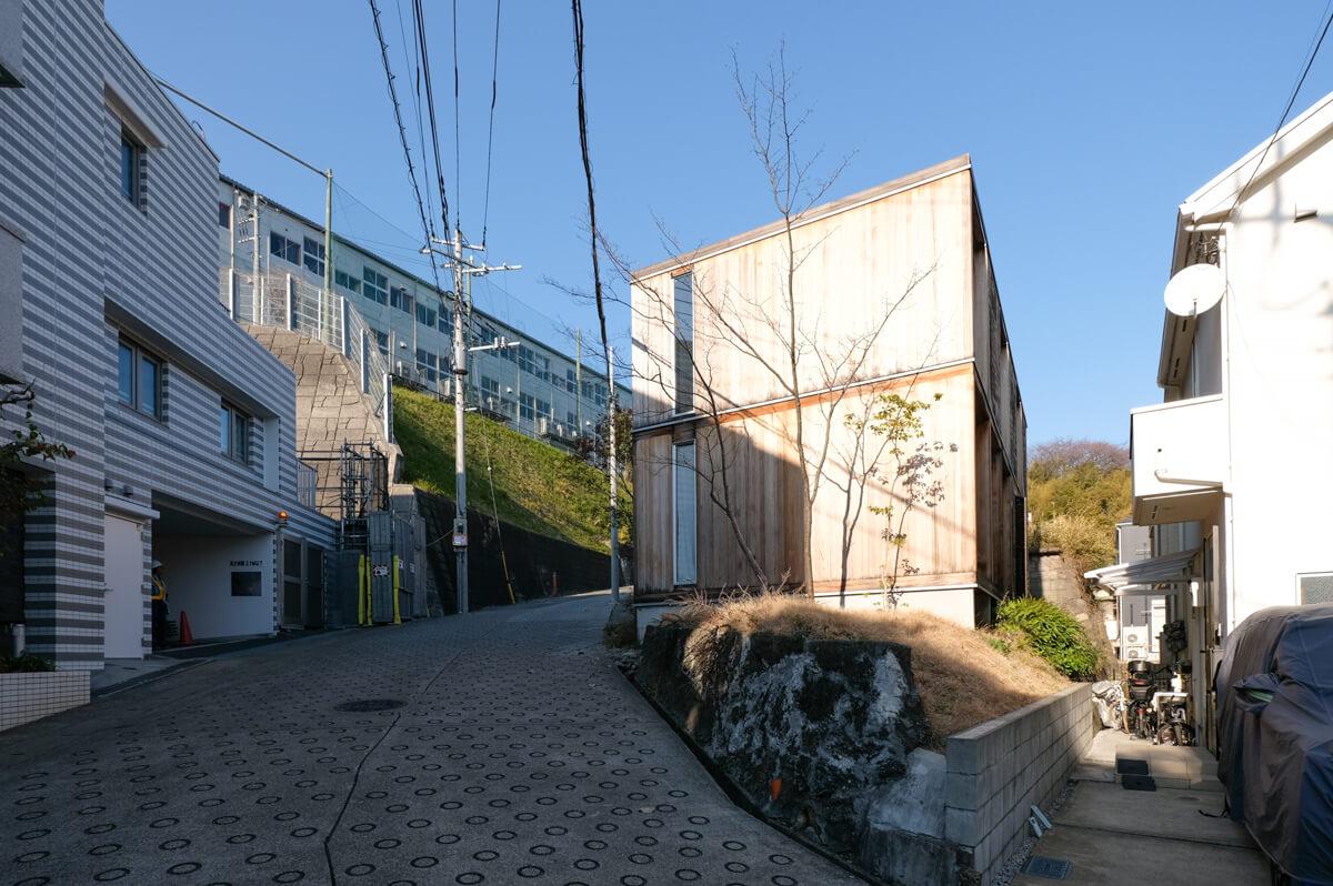 神奈川県横浜市港北区菊名の売買物件/坂の途中から見上げた外観（側面はヒバ・縦）。木という素材だけでも経年変化によって豊かな表情が生まれますが、植栽も含めて街の風景になることを目指しています。
