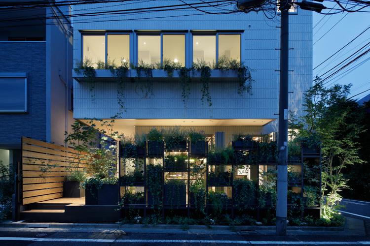 通りに面して植栽の棚が並ぶ。玄関とは別に左手のウッドデッキからアトリエに入ることもできる