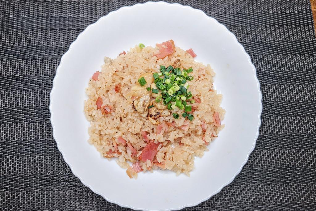 【絶品すぎるガーリックライス】 ①フライパンにバターを入れ弱火でベーコン、にんにくを炒め、にんにくに焼き色がついたらごま油を入れる ②ベーコンに火が通ったらごはん、めんつゆ、鶏ガラの素、ブラックペッパーを混ぜ、皿に移してネギをのせて完成