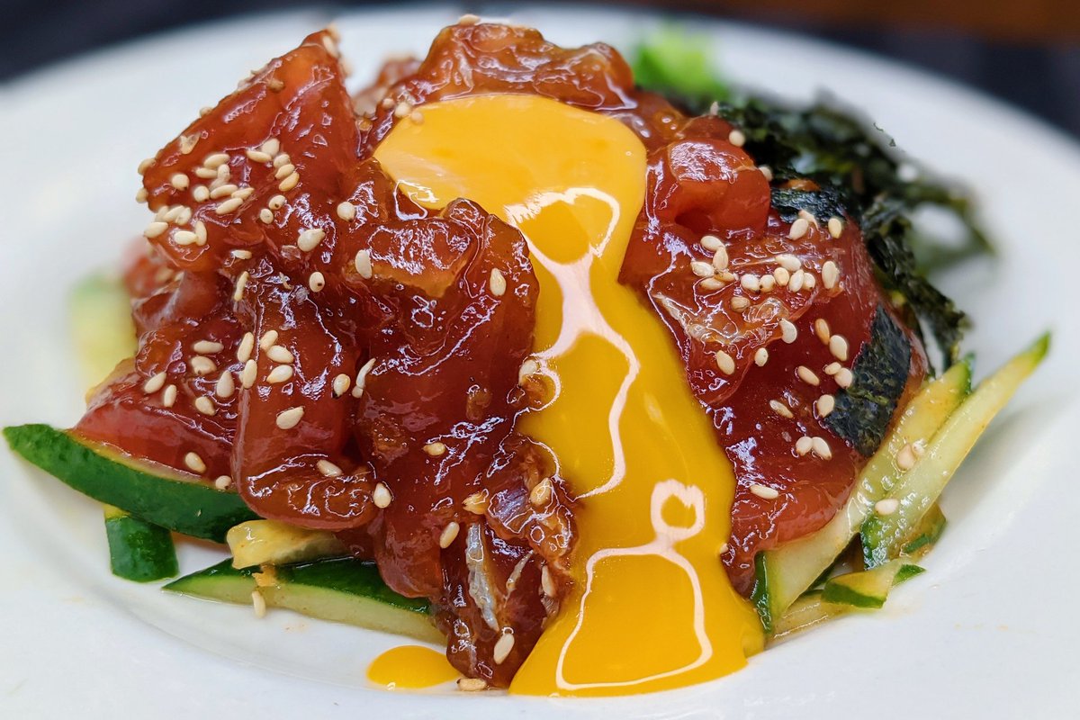 まぐろユッケ】  ①マグロをカットし、醤油、ごま油、コチュジャン、にんにく、生姜を混ぜ10分おく ②白ごまを加えてきゅうりの上にのせ卵黄、ネギ、のりをのせれば完成