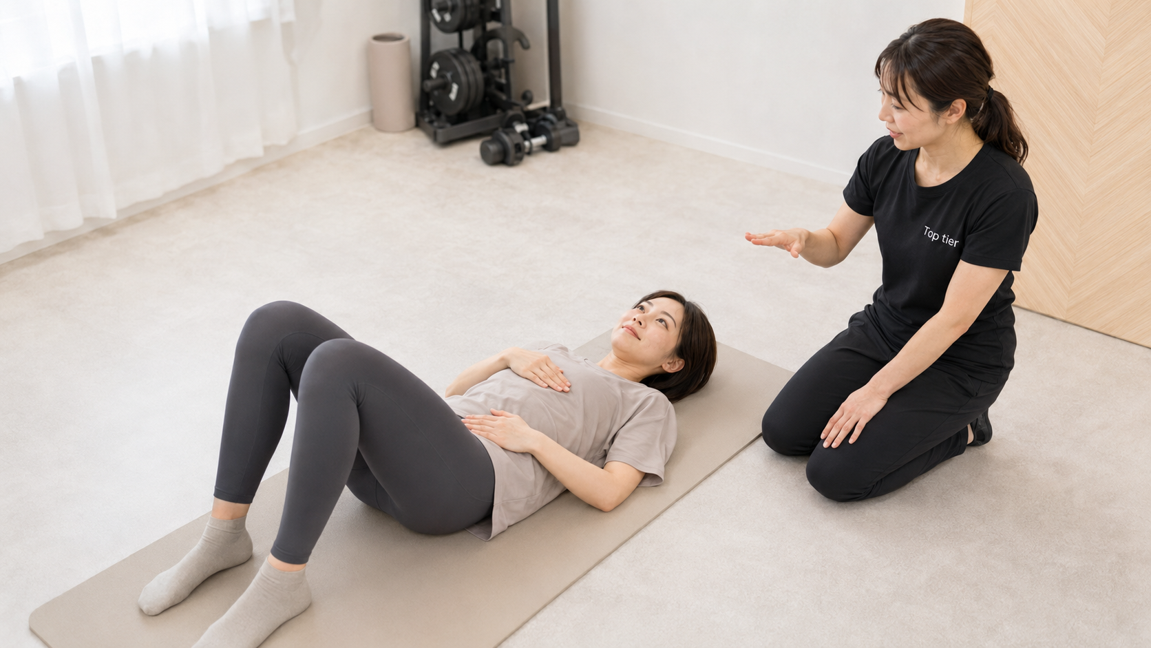 女性専用パーソナルジムで、産後の女性がトレーナーの指導を受けながら呼吸と腹部の使い方を確認する様子