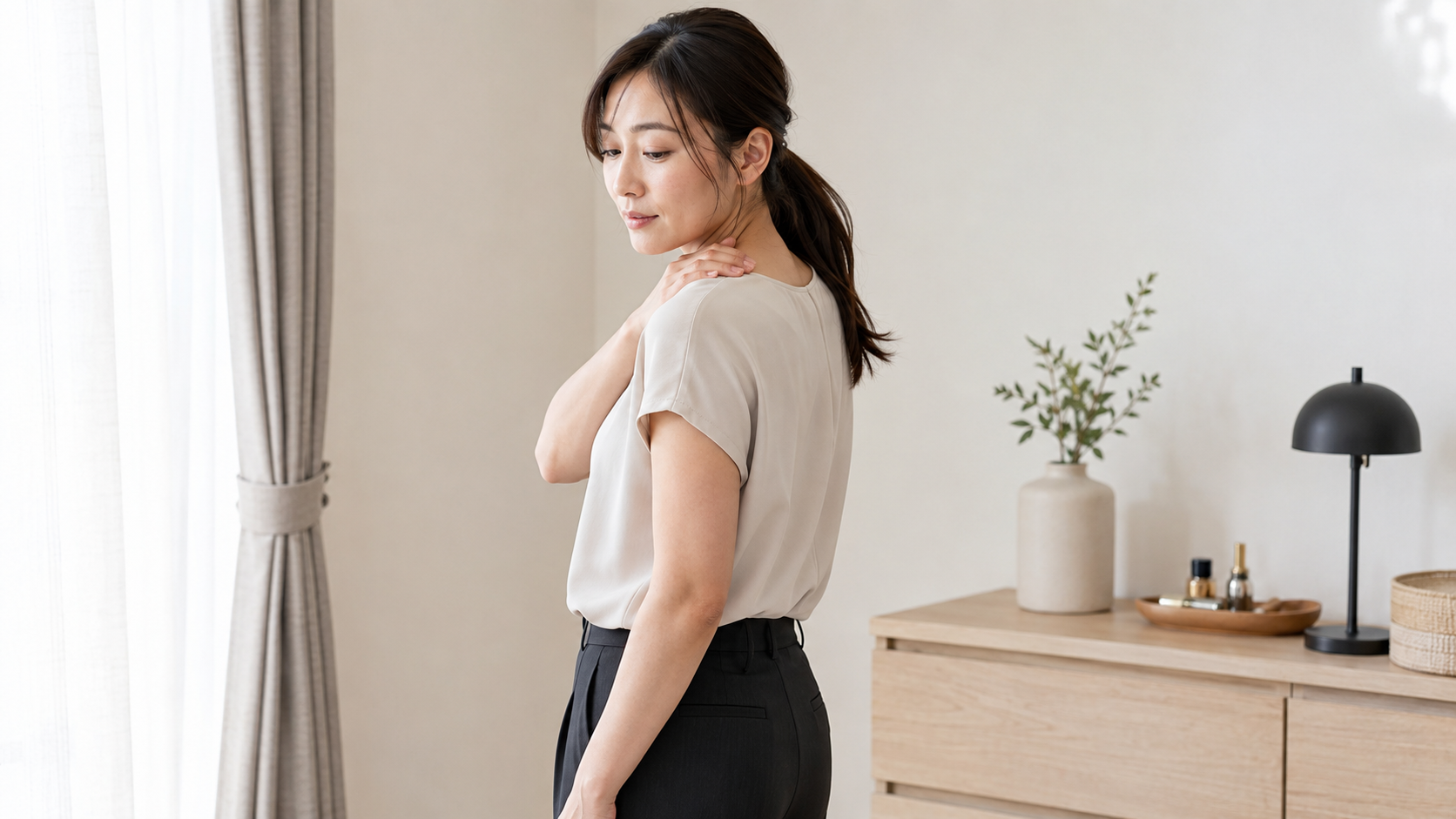 普段着の女性が首と肩に手を添え、巻き肩による二の腕・背中の見え方と首肩への影響を表した写真