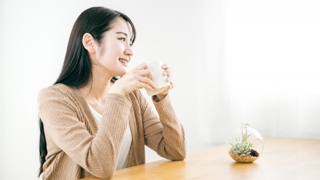 温かい飲み物を手に、穏やかな表情で一息つく女性。自分一人の時間を大切にする休息のイメージ。