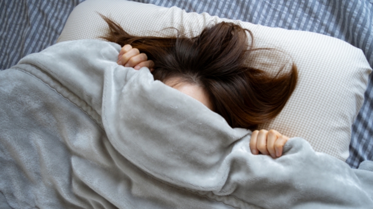 生理前の体のだるさやイライラ、頭痛などのPMS症状に布団をかぶって悩む女性のイメージ