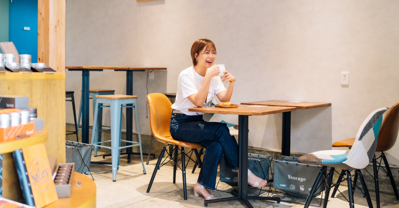 スペシャルティコーヒーのカフェバー「7Story.co shinjuku」の店内。木のテーブルと椅子が並ぶ明るい空間で、来店客がコーヒーカップを手に笑っている