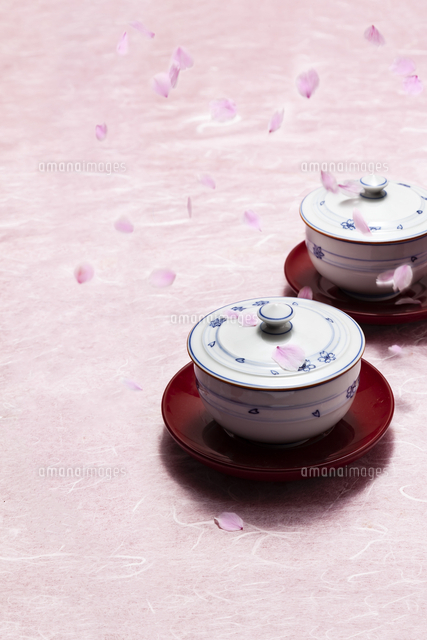 ピンクの和紙の上にあるお茶碗に落下している桜の花びら 10147000644