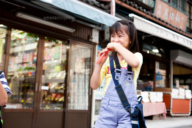 駄菓子屋の前で駄菓子を食べる女の子 の写真素材 イラスト素材 アマナイメージズ