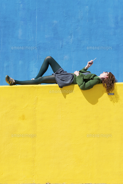 Side view of businesswoman using smart phone while lying on yellow wall during sunny day
(c)Cavan Social