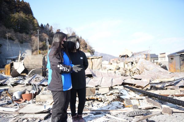 全焼した自宅の前で友人と話す東川樺恩さん(左)