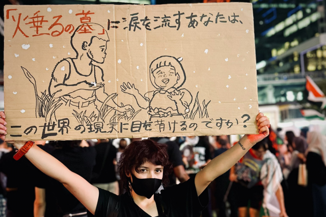《「火垂るの墓」に涙を流すあなたは、この世界の現実に目を背けるのですか？》。パレスチナ自治区ガザに連帯する集会で、プラカードを掲げる参加者＝2025年8月3日、東京都渋谷区、さくらさん提供