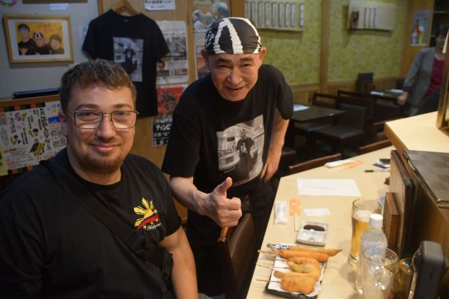 アメリカ・フロリダからやってきたという男性（左）と吉岡富佐男さん。私は手元の紙を使って筆談でインタビューをした。馬刺しを初めて食べたあと、男性は顔をゆがませていた