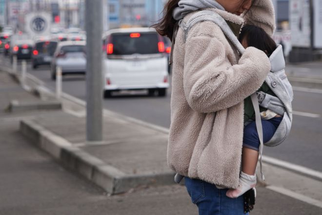 胸に次女を抱く女性。生活保護の申請後、持っている車の処分を求められました=2025年2月、東北地方、小玉重隆撮影