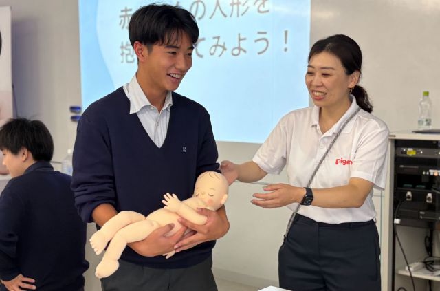 スタッフに教えられながら赤ちゃんの人形を抱く生徒