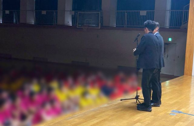 体育館のステージで生徒に漫才を披露する「キクバリ」＝キクバリ提供、画像の一部を加工しています