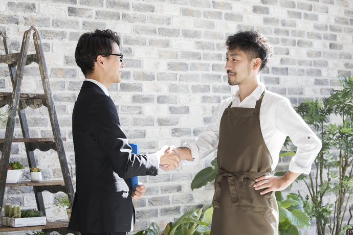 握手を交わすエプロン姿の男性とスーツの男性